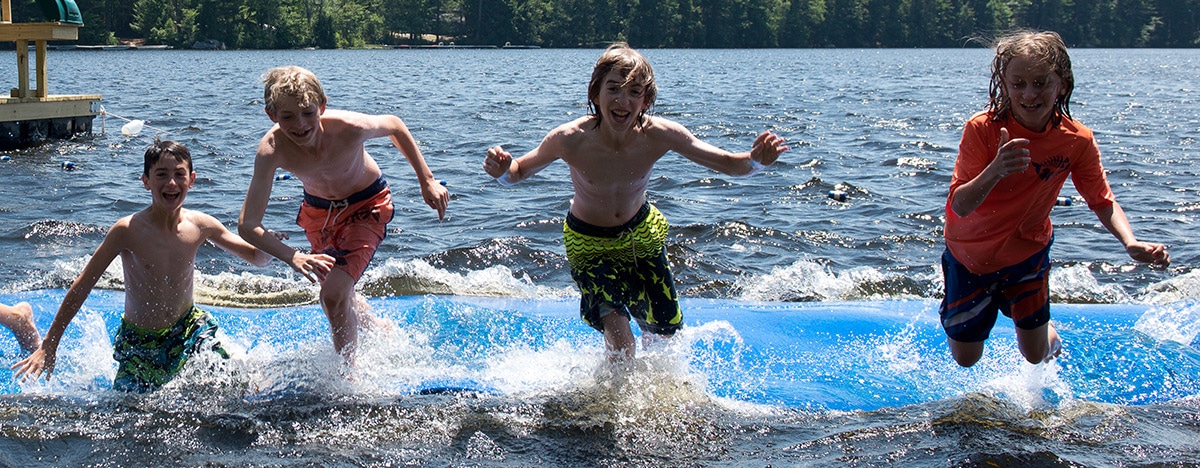 Windsor Mountain campers jumping off the water mat into the cool lake on a warm summer day in New Hampshire
